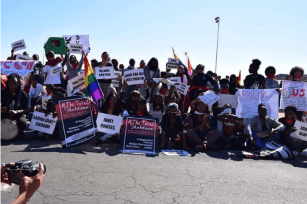 Group photo of protestors. Many different illegible signs being held up in the photo. 